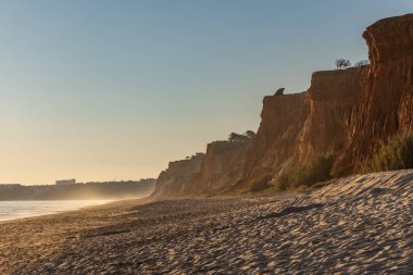 Atlantik 'te kumlu bir sahil. Kum taşı kayalıkları olan bir sahilin gün batımında manzara. Albufeira, Algarve, Portekiz yakınlarındaki Praia da Falsia 'nın sarı sahilinde gelgit var.