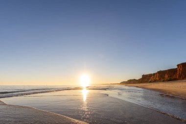 Alçak gelgitte kumlu bir sahil manzarası. Gün batımında etrafındaki kayalar ve kayalıklar denize yansıyor. Praia da Falsia, Algarve, Portekiz