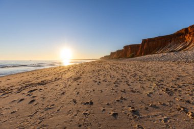 Atlantik 'te kumlu bir sahil. Kum taşı kayalıkları olan bir sahilin gün batımında manzara. Albufeira, Algarve, Portekiz yakınlarındaki Praia da Falsia 'nın sarı sahilinde gelgit var.