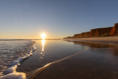 Alçak gelgitte kumlu bir sahil manzarası. Gün batımında etrafındaki kayalar ve kayalıklar denize yansıyor. Praia da Falsia, Algarve, Portekiz