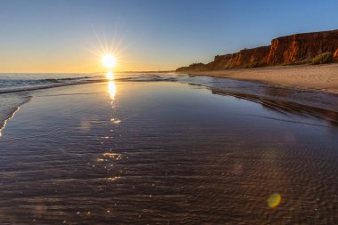 Alçak gelgitte kumlu bir sahil manzarası. Gün batımında etrafındaki kayalar ve kayalıklar denize yansıyor. Praia da Falsia, Algarve, Portekiz