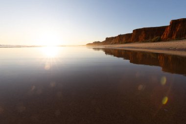 Alçak gelgitte kumlu bir sahil manzarası. Gün batımında etrafındaki kayalar ve kayalıklar denize yansıyor. Praia da Falsia, Algarve, Portekiz