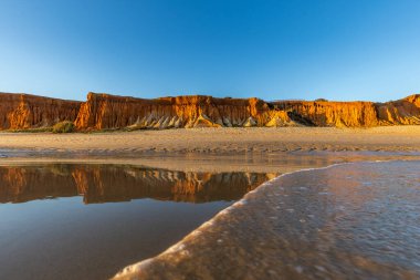 Alçak gelgitte kumlu bir sahil manzarası. Gün batımında etrafındaki kayalar ve kayalıklar denize yansıyor. Praia da Falsia, Algarve, Portekiz