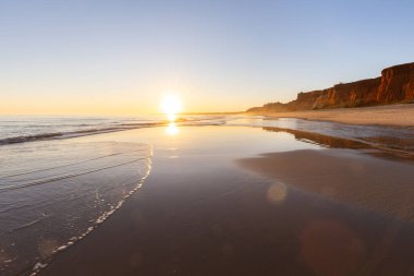 Alçak gelgitte kumlu bir sahil manzarası. Gün batımında etrafındaki kayalar ve kayalıklar denize yansıyor. Praia da Falsia, Algarve, Portekiz