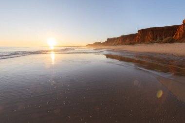 Alçak gelgitte kumlu bir sahil manzarası. Gün batımında etrafındaki kayalar ve kayalıklar denize yansıyor. Praia da Falsia, Algarve, Portekiz