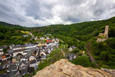 Dağlar ve şatoyla çevrili nehir kıyısındaki yarı keresteli bir köyün manzarası. Almanya 'nın Elzbach kentindeki Monreal şehrinin güzel doğası
