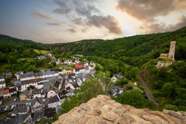 Dağlar ve şatoyla çevrili nehir kıyısındaki yarı keresteli bir köyün manzarası. Almanya 'nın Elzbach kentindeki Monreal şehrinin güzel doğası