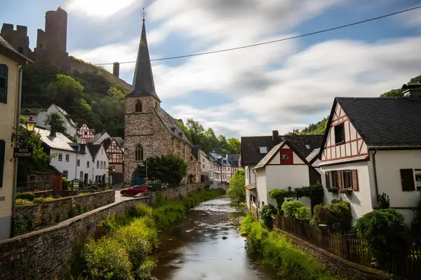 Dağlar ve şatoyla çevrili nehir kıyısındaki yarı keresteli bir köyün manzarası. Almanya 'nın Elzbach kentindeki Monreal şehrinin güzel doğası