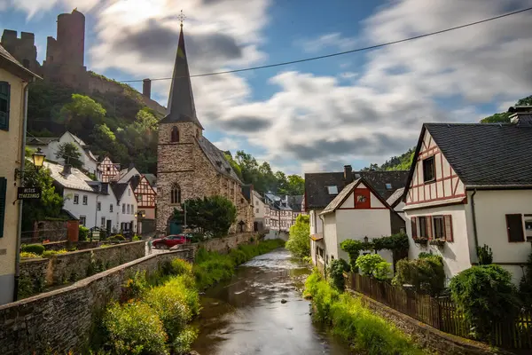 Dağlar ve şatoyla çevrili nehir kıyısındaki yarı keresteli bir köyün manzarası. Almanya 'nın Elzbach kentindeki Monreal şehrinin güzel doğası