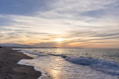 Gün batımında kumlu ve çakıl taşı plajı olan güzel bir sahil şeridi. Platanes Beach, Rethymno, Girit, Yunanistan 'ın turizm ve otel bölgesinde güzel gökyüzü renklendirmesi