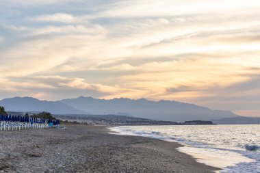 Gün batımında kumlu ve çakıl taşı plajı olan güzel bir sahil şeridi. Platanes Beach, Rethymno, Girit, Yunanistan 'ın turizm ve otel bölgesinde güzel gökyüzü renklendirmesi