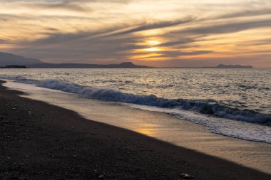 Gün batımında kumlu ve çakıl taşı plajı olan güzel bir sahil şeridi. Platanes Beach, Rethymno, Girit, Yunanistan 'ın turizm ve otel bölgesinde güzel gökyüzü renklendirmesi