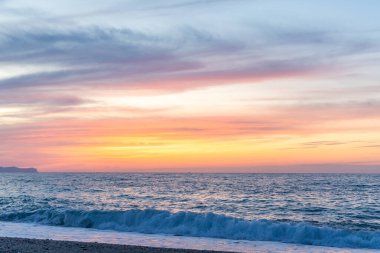 Gün batımında kumlu ve çakıl taşı plajı olan güzel bir sahil şeridi. Platanes Beach, Rethymno, Girit, Yunanistan 'ın turizm ve otel bölgesinde güzel gökyüzü renklendirmesi