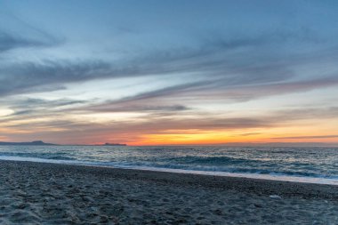 Gün batımında kumlu ve çakıl taşı plajı olan güzel bir sahil şeridi. Platanes Beach, Rethymno, Girit, Yunanistan 'ın turizm ve otel bölgesinde güzel gökyüzü renklendirmesi