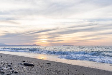 Gün batımında kumlu ve çakıl taşı plajı olan güzel bir sahil şeridi. Platanes Beach, Rethymno, Girit, Yunanistan 'ın turizm ve otel bölgesinde güzel gökyüzü renklendirmesi