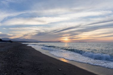 Gün batımında kumlu ve çakıl taşı plajı olan güzel bir sahil şeridi. Platanes Beach, Rethymno, Girit, Yunanistan 'ın turizm ve otel bölgesinde güzel gökyüzü renklendirmesi