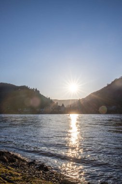 Nehir kenarındaki tepelerde gün batımı. Güneş tepelerin ve üzüm bağlarının üzerinde parlıyor ve nehre yansıyor. Ren 'den Almanya' nın Bacharach kasabasına bakın..