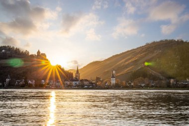 Nehir kenarındaki tepelerde gün batımı. Güneş tepelerin ve üzüm bağlarının üzerinde parlıyor ve nehre yansıyor. Ren 'den Almanya' nın Bacharach kasabasına bakın..