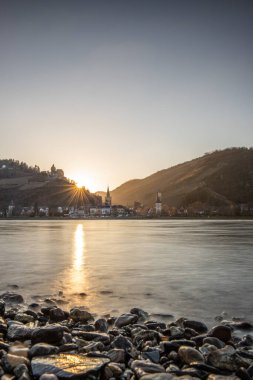 Nehir kenarındaki tepelerde gün batımı. Güneş tepelerin ve üzüm bağlarının üzerinde parlıyor ve nehre yansıyor. Ren 'den Almanya' nın Bacharach kasabasına bakın..