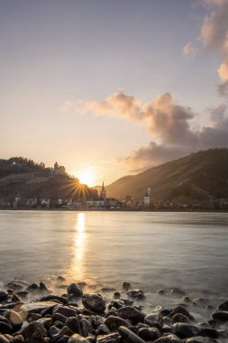 Nehir kenarındaki tepelerde gün batımı. Güneş tepelerin ve üzüm bağlarının üzerinde parlıyor ve nehre yansıyor. Ren 'den Almanya' nın Bacharach kasabasına bakın..