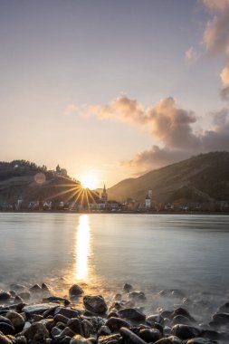 Nehir kenarındaki tepelerde gün batımı. Güneş tepelerin ve üzüm bağlarının üzerinde parlıyor ve nehre yansıyor. Ren 'den Almanya' nın Bacharach kasabasına bakın..