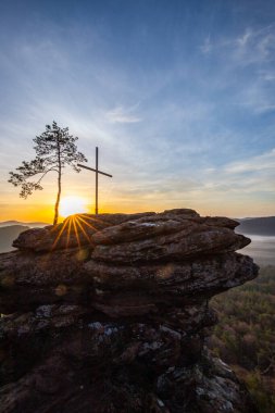 Bir dağ manzarasında gün doğumu. Ormandaki kumtaşı bir uçurumun arkasında yükselen güneş. Almanya 'daki Rtzenfelsen, Palatinate Ormanı' ndaki vadide sis oluşuyor.