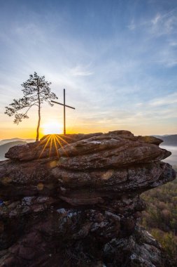 Bir dağ manzarasında gün doğumu. Ormandaki kumtaşı bir uçurumun arkasında yükselen güneş. Almanya 'daki Rtzenfelsen, Palatinate Ormanı' ndaki vadide sis oluşuyor.