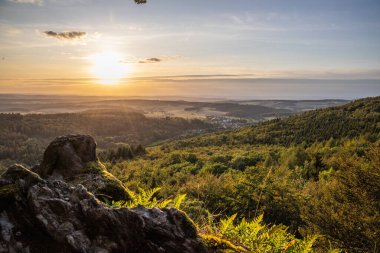 Taunus, Almanya 'da Feldberg' de güzel bir günbatımı. Doğada harika bir manzarayla ön planda bir taş ve yeşillik fotoğrafı çekildi.