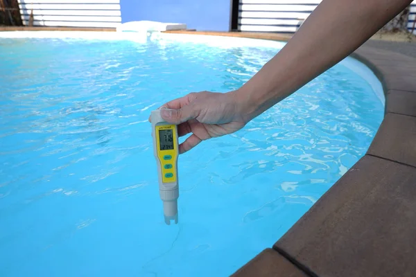 Digital water testing in female hand on swimming pool  background,  ph check for water quality control.