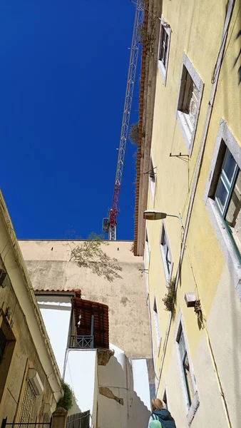 stock image Behind the old walls of the house you can see a construction crane against the blue sky in Lisbon. High quality photo