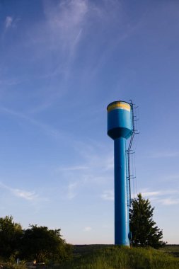 Mavi bir su kulesi, yeşil bir çimenliğin ortasında mavi bir gökyüzüne karşı. Yerleşim yerine temiz su sağlamak için. Çok derinlerdeki bir kuyudan temiz içme suyu pompalamak için.