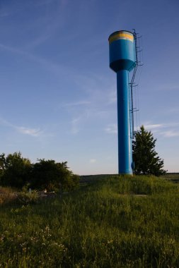 Mavi bir su kulesi, yeşil bir çimenliğin ortasında mavi bir gökyüzüne karşı. Yerleşim yerine temiz su sağlamak için. Çok derinlerdeki bir kuyudan temiz içme suyu pompalamak için.