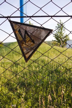 Eski çitlerde, yoldan geçenleri tehlikeyle ilgili uyaran metal bir ağa asılı bir tabela var. Çitlere enerji veriliyor ve bir insan elektrik çarpması riskiyle karşı karşıya.