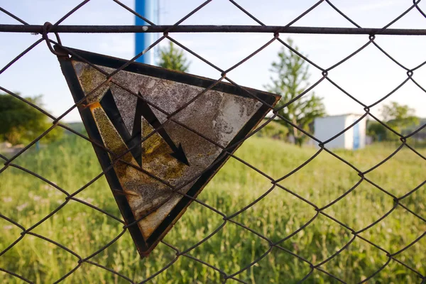 On the old fence, a sign hangs from a metal mesh that warns passers-by about the danger - the fence is energized and a person risks being electrocuted