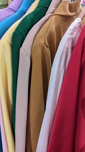 A Chinese store in Lisbon has a lot of clothes in different colors on hangers. On a hanger in a clothing store hang colorful shirts and jackets on hangers in a row
