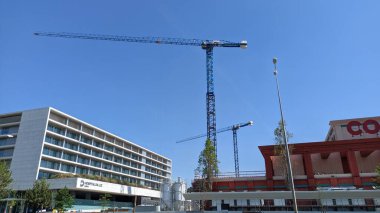 27.03.2023 Uzun bir vinç mavi gökyüzüne karşı bir inşaat sahasında çalışıyor