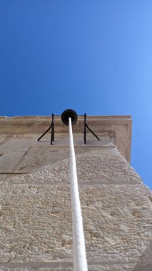 Evin duvarında büyük siyah metal bir çan ve kalın beyaz bir ip resmi var.