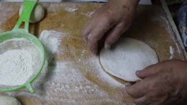 Geleneksel bir yemek tarifi hazırlamak için bir tahta kesme tahtasının üzerinde bir parça hamur dilimliyor. Tabakta İran limonu ve limon gibi yaprak sebzeler ve narenciye meyveleri yer alıyor.