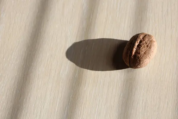 A walnut, a staple food ingredient in many cuisines, is placed on a wooden table, ready to be used in dishes, baked goods, and as a nutritious snack