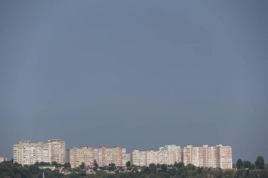 Dramatik ve bulutlu bir gökyüzüne karşı inşa edilmiş uzun şehir binalarının geniş manzaralı bir alacakaranlık sahnesi.