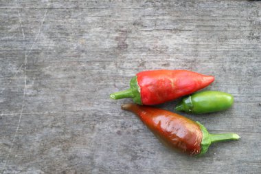 Kırsal ahşap bir yüzeye dizilmiş canlı kırmızı ve yeşil acı biberler görsel olarak çekici bir sahne yaratıyor.