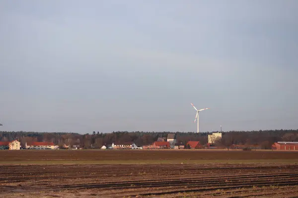stock image A picturesque rural landscape showcases a wind turbine, vast farmland, and clear skies under a panoramic view