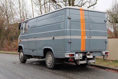 Geleneksel mavi minibüs, klasik dağıtım aracını tasvir eden sakin caddede park edilmiş turuncu çizgili.