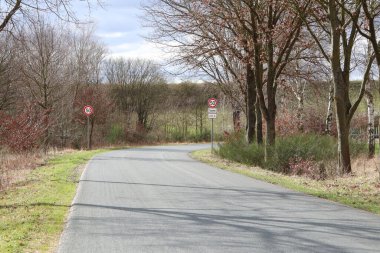 Kırsal bir yol, ağaçlar, çalılar, hız limiti işaretleri ve sakin bir günde bulutların olduğu sakin bir kırsal bölge.
