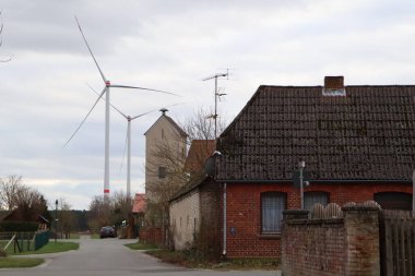 Rüzgâr türbinlerinin ve kırsal atmosferde tuhaf evlerin bulunduğu sakin bir köy bulutlu bir gökyüzüne karşı kurulmuş.
