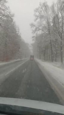 Karla kaplı yol çıplak ağaçlarla çevrili, kış havasında araba sürüyor, sakin ve sakin bir atmosfer.