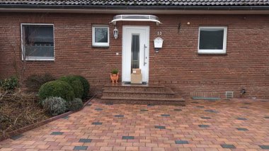 Üzerinde el değmemiş beyaz bir kapı bulunan büyüleyici tuğladan bir ev, yanında da tam önünde bulunan iyi korunmuş tuğladan bir garaj yolu.