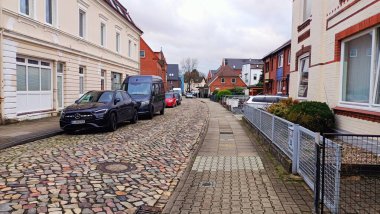 Yan tarafa park etmiş çeşitli arabaların bulunduğu büyüleyici bir kaldırım taşı caddesi, ona hoş ve güzel bir his veriyor.
