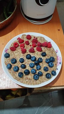 Kırsal bir ahşap masada taze ahududu ve yaban mersiniyle kaplanmış güzel bir tabak yulaf ezmesi var.