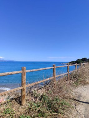 Göz kamaştırıcı bir okyanus manzarası büyüleyici ahşap bir çiti sergiliyor yukarıda canlı mavi bir gökyüzüne karşı.